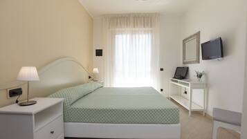 A bedroom with a bed, bedside tables, a lamp, a TV, and a desk with a chair.