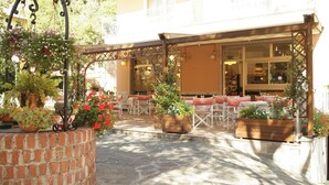 A covered outdoor seating area with brick walls, potted plants, and a café setting. - Residence Kriss (Deiva Marina)