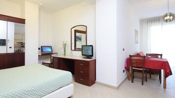 A bedroom with a bed, a desk with a computer, a mirror, and a dining table with chairs.
