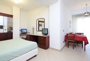 Ein Schlafzimmer mit einem Bett, einem Schreibtisch mit Computer, einem Spiegel und einem Esstisch mit Stühlen.