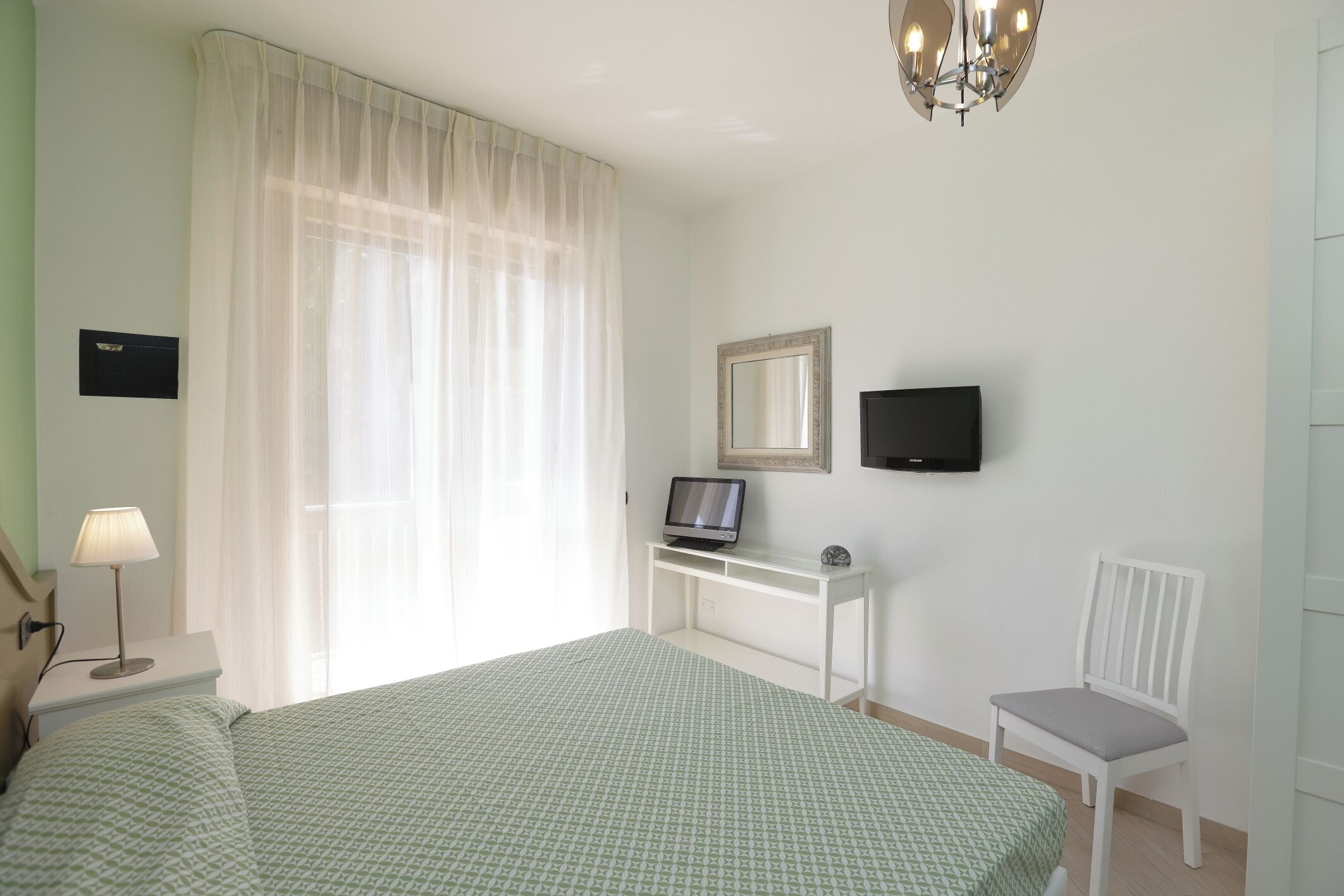 Une chambre d’hôtel avec un lit, un bureau avec un ordinateur, une chaise, une télévision et une fenêtre avec des rideaux.