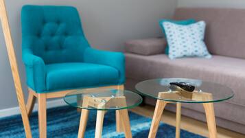Un sillón azul aguamarina, una mesa de centro de vidrio y un sofá beige con un cojín estampado en una sala de estar.