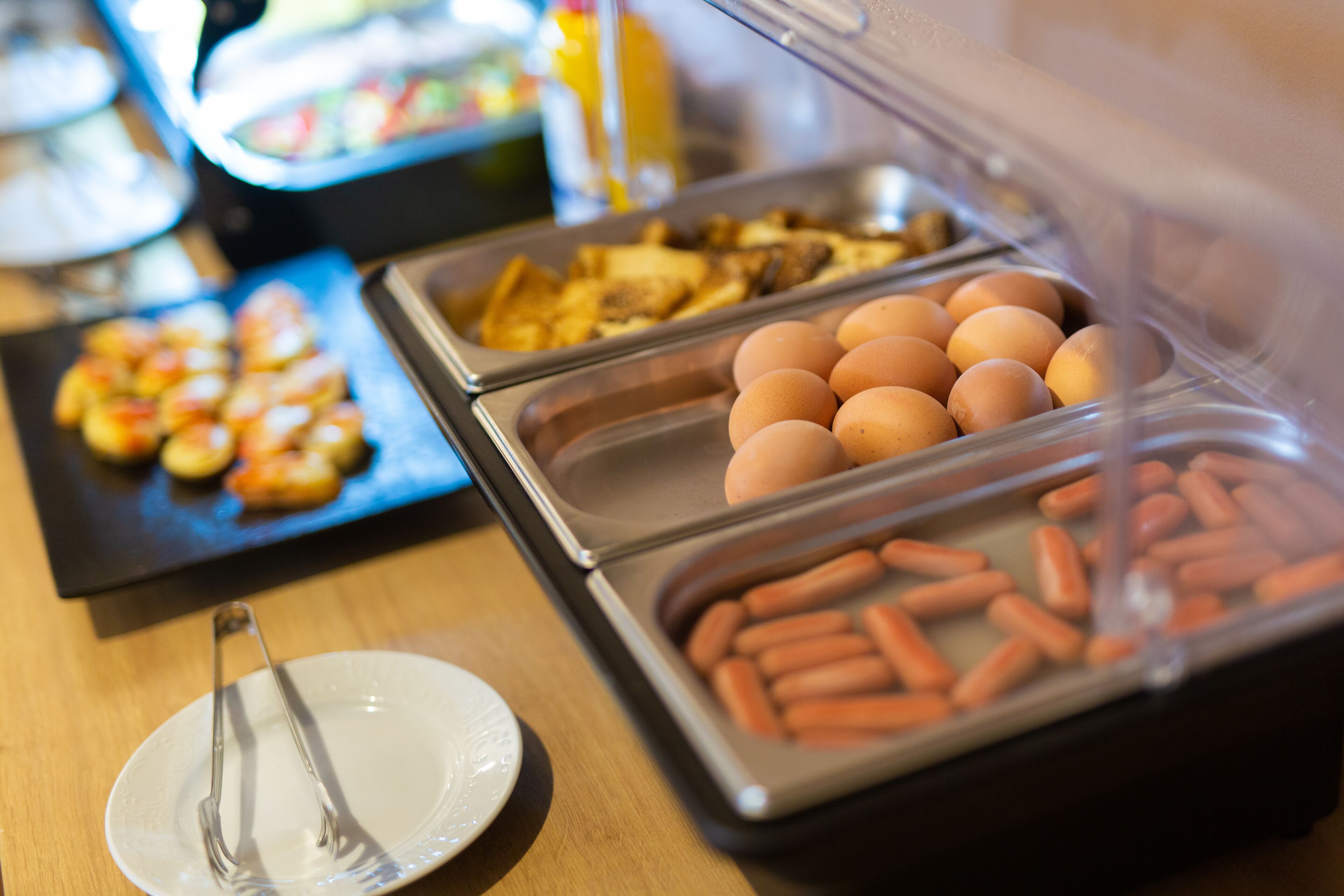 Un buffet proposant une variété de plats, notamment des œufs, des saucisses et des viennoiseries.