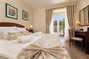Habitación de hotel con una cama grande, un escritorio, una silla y un balcón con cortinas.