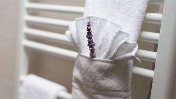 Una toalla blanca con una flor de lavanda en un sujetatowelas blanco sobre un radiador blanco.