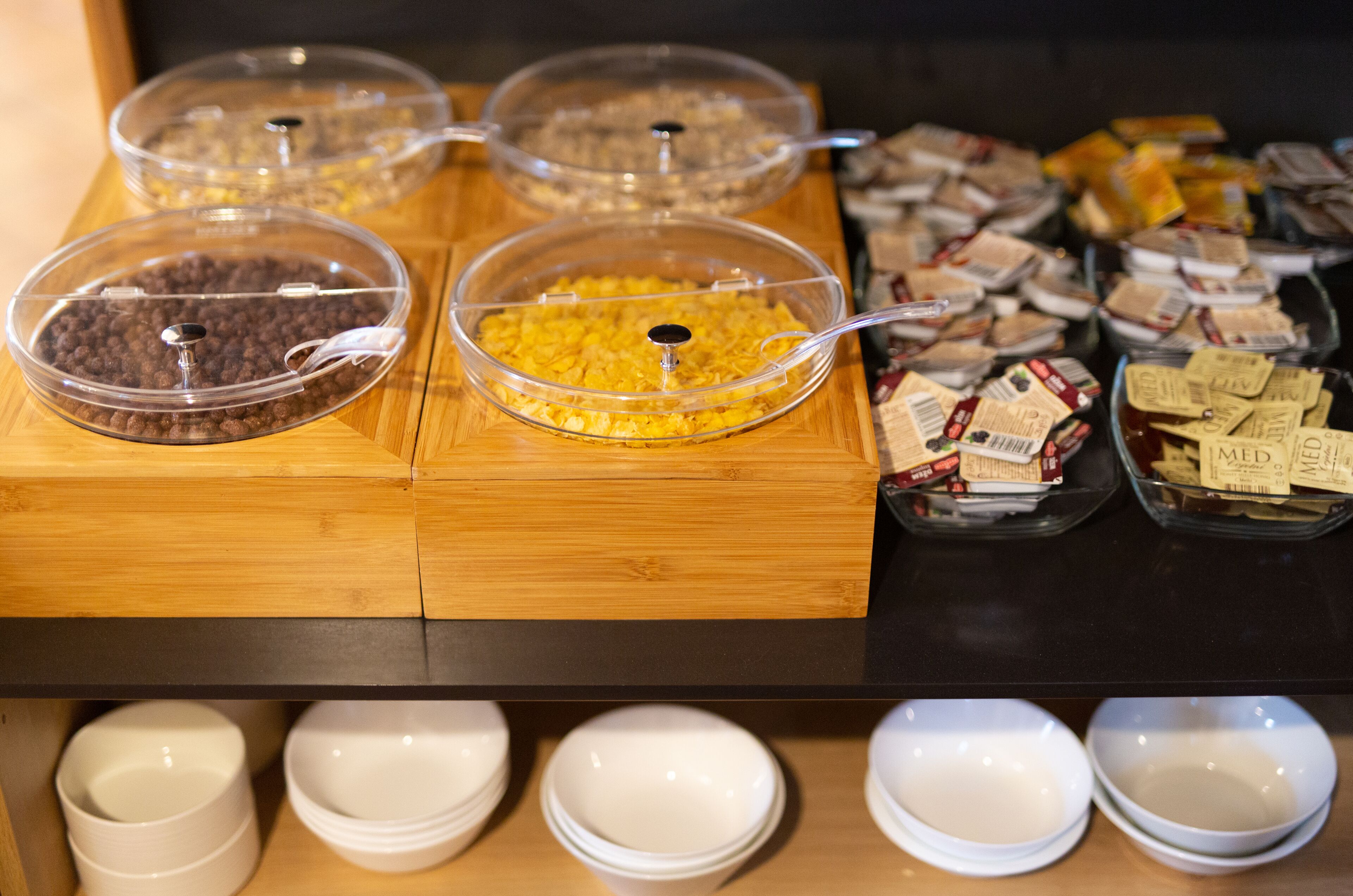 Een buffet met verschillende soorten eten in transparante bakken, waaronder ontbijtgranen en snacks.