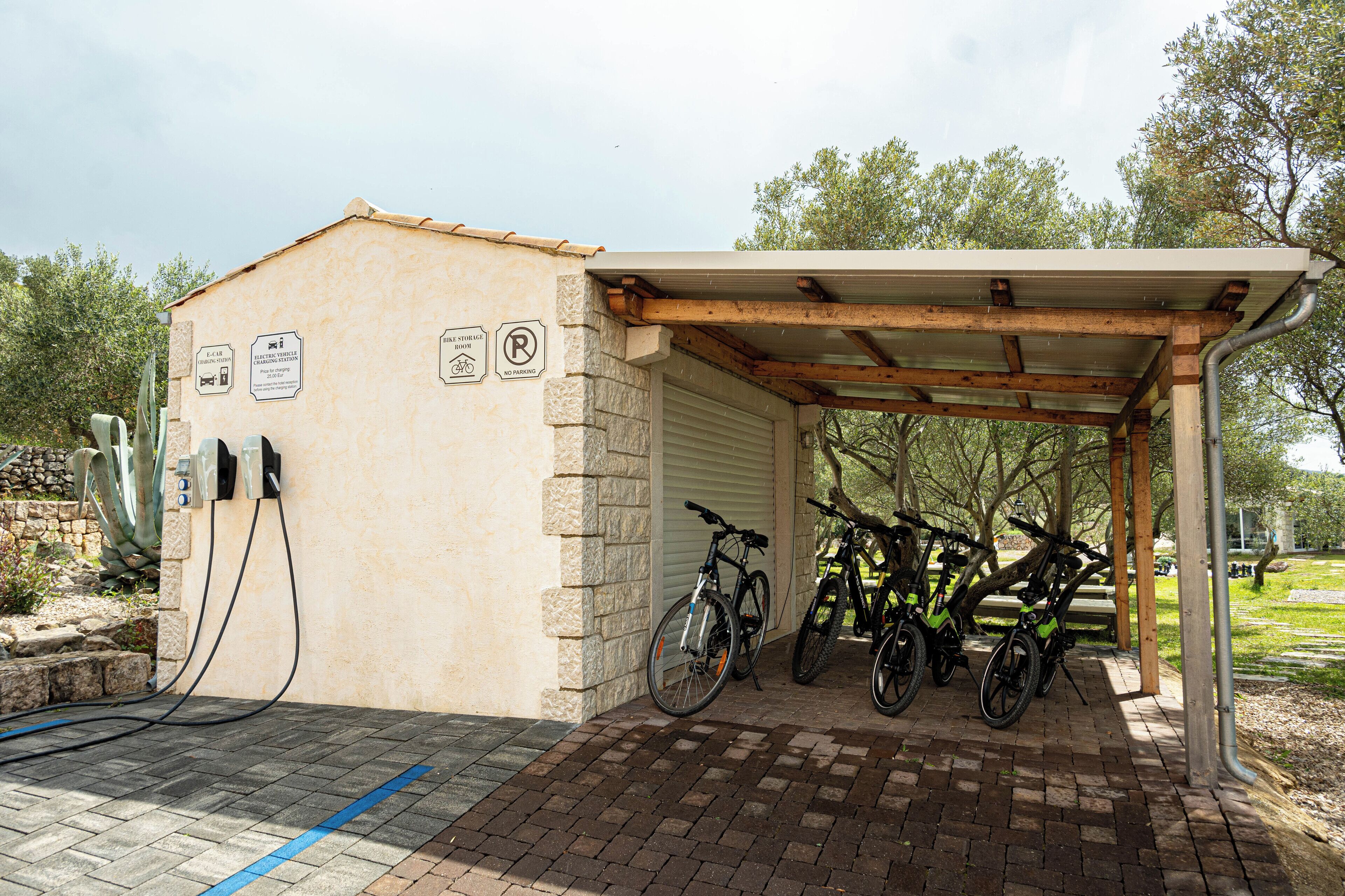 Zona de estacionamiento cubierto para bicicletas con estaciones de carga para vehículos eléctricos y un camino de ladrillo.