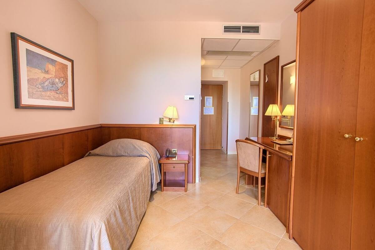 Una habitación de hotel con cama, mesita de noche, lámpara y armario.
