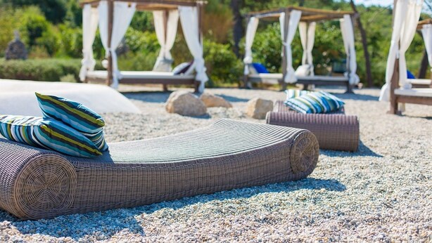 A beachside lounge area with wicker loungers, pillows, and a pebbled ground. - Hotel Kanajt (Punat)