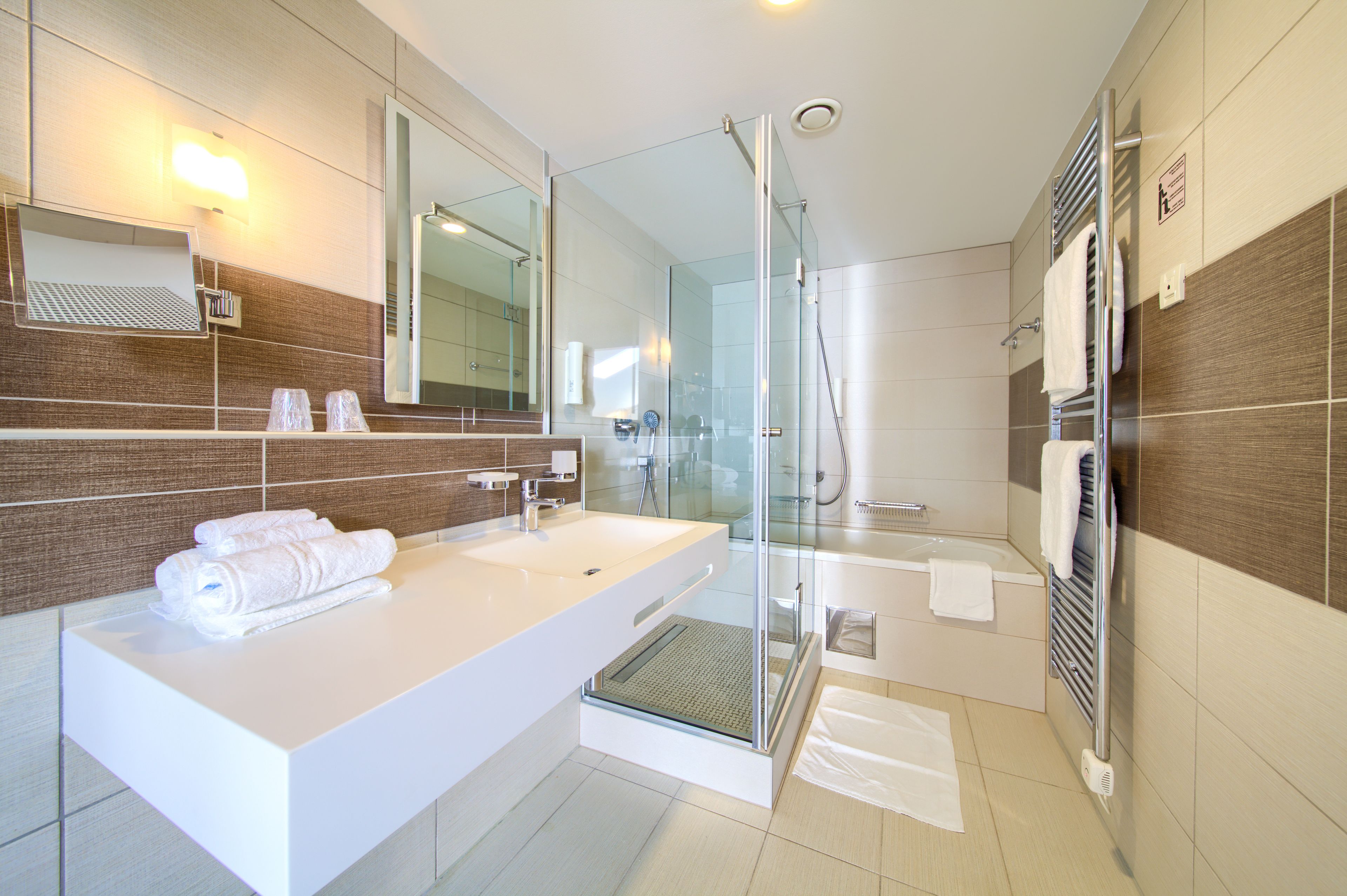 Un baño moderno con un espejo grande, lavamanos blanco y cabina de ducha con paredes de vidrio.