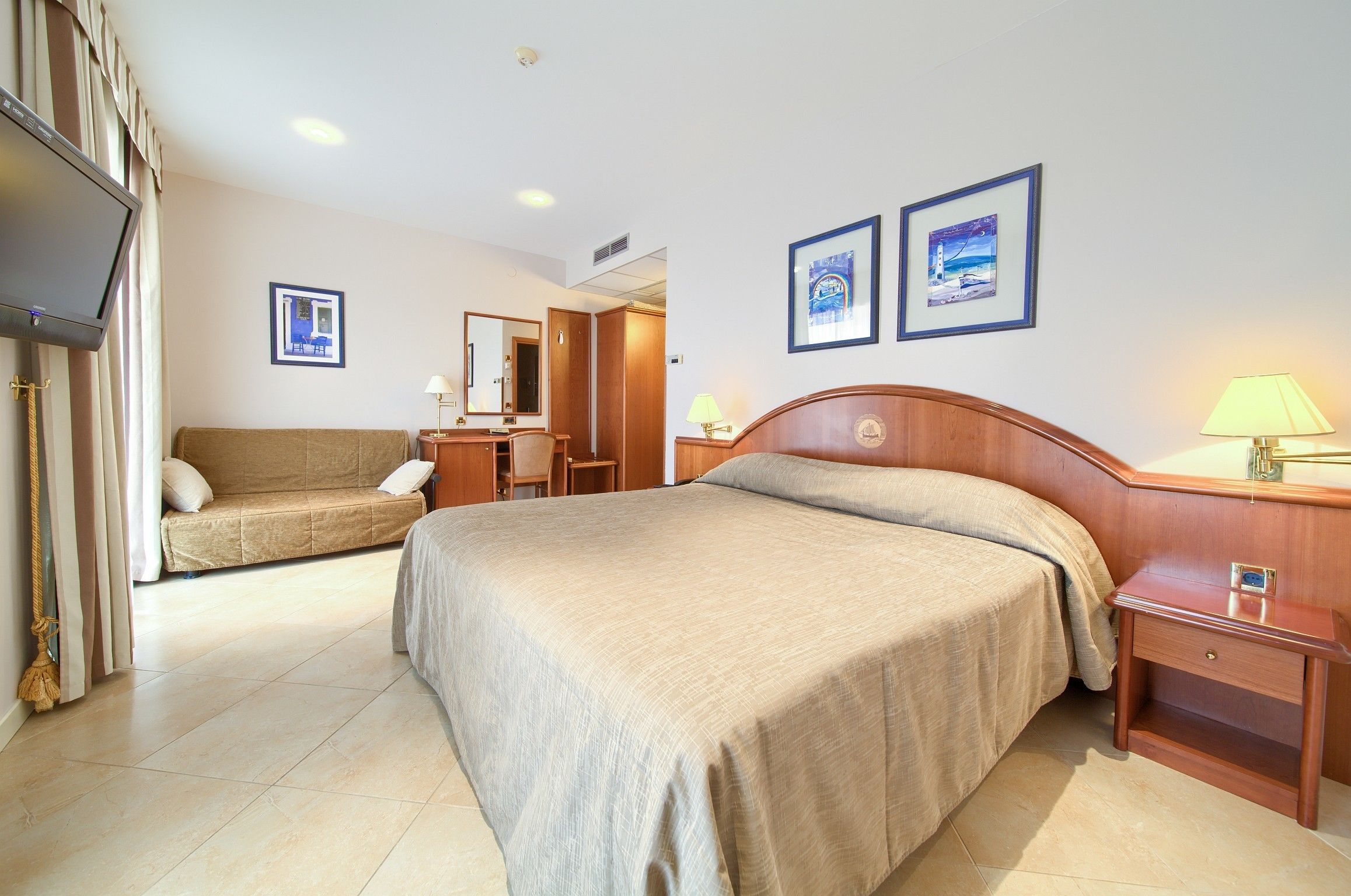A hotel room with a bed, a sofa, a desk, and a television.