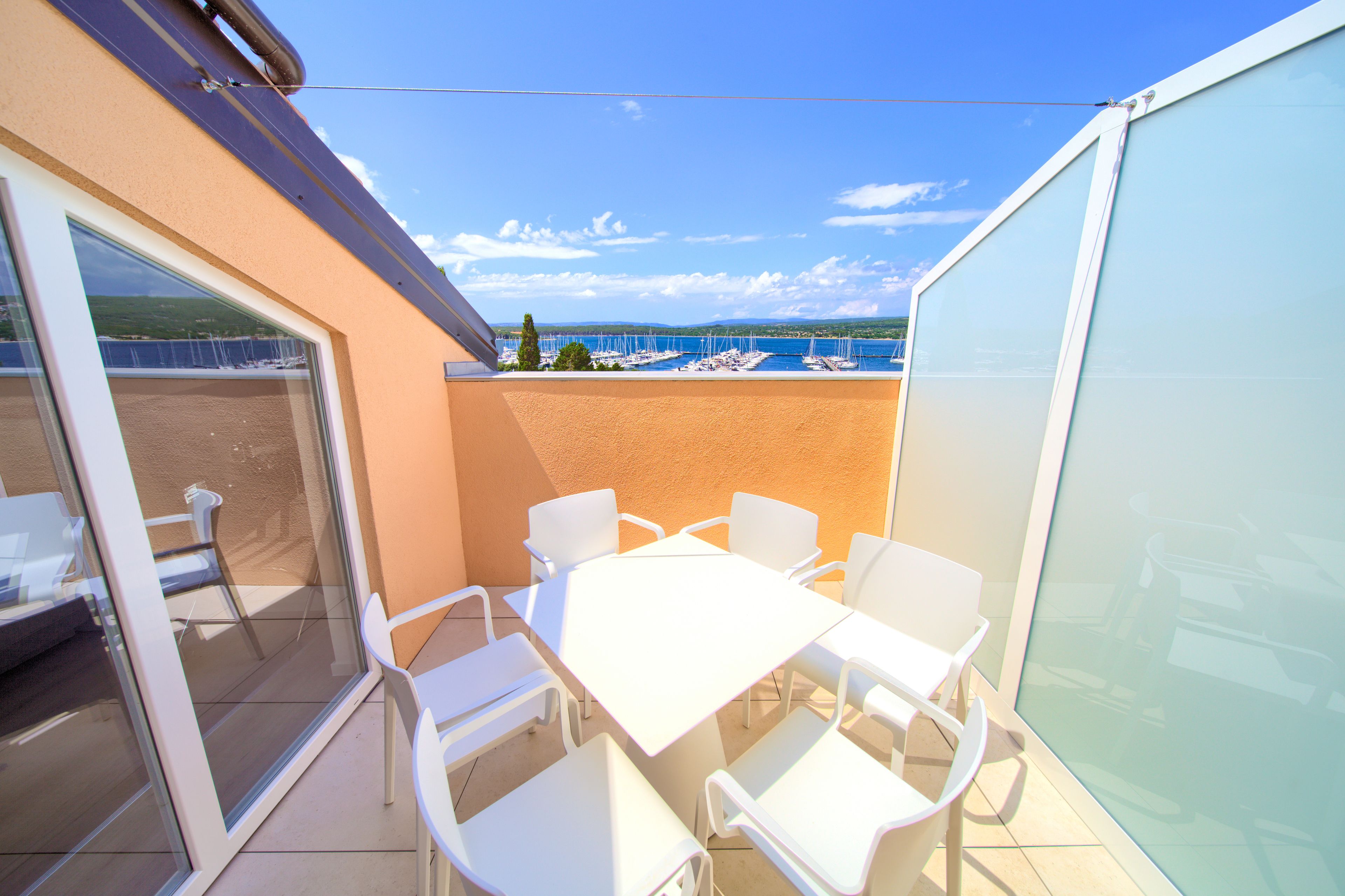 Ein Balkon mit Tisch und Stühlen, eine Glastür und Blick auf Boote auf dem Wasser.