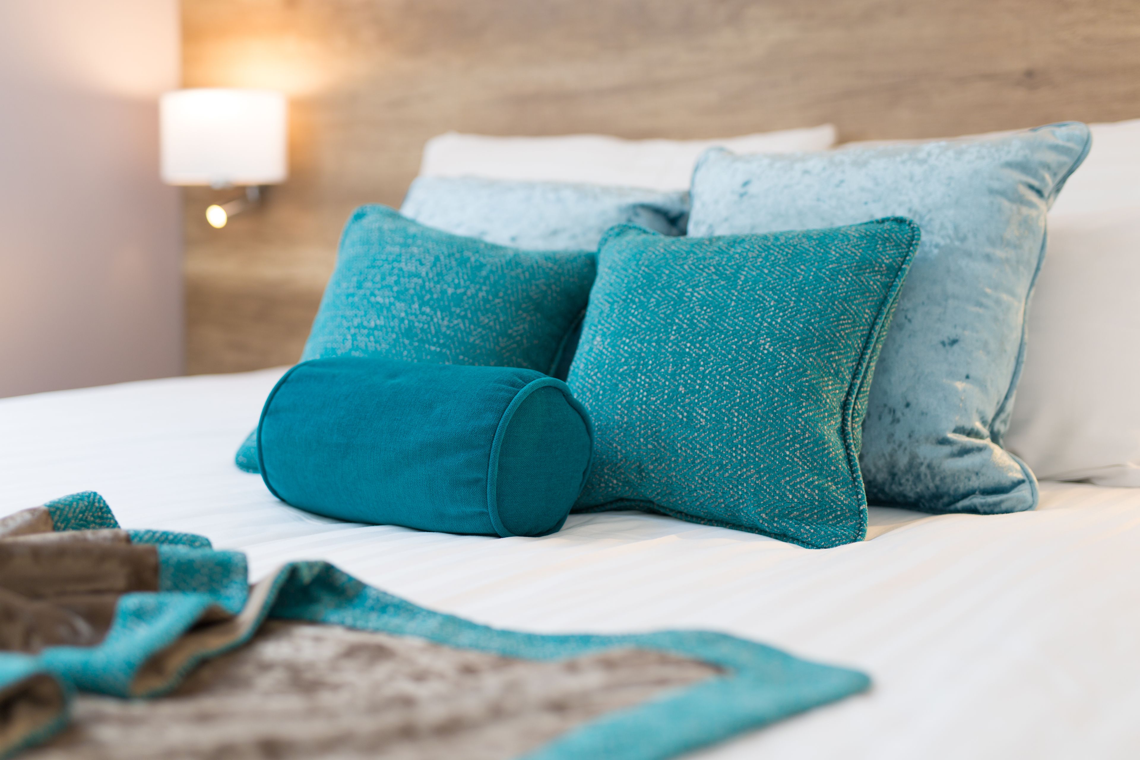 A neatly made bed with teal pillows and a blanket.