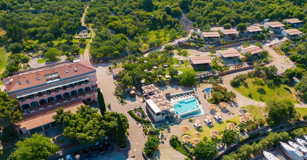 Vista aérea de un complejo turístico con varias edificaciones, una piscina y abundante vegetación.
