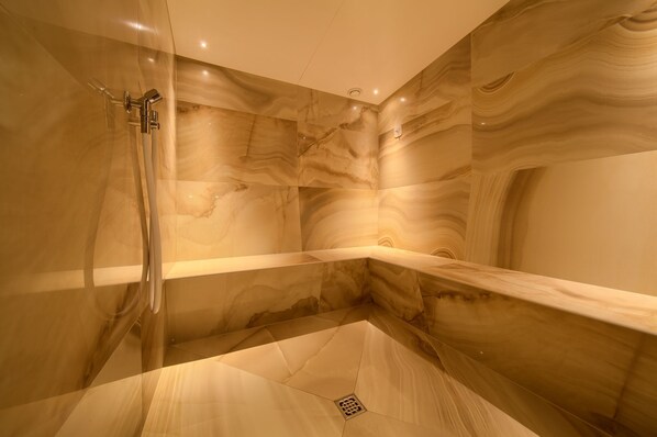A modern bathroom with a glass-enclosed shower, marble walls, and a built-in bench.