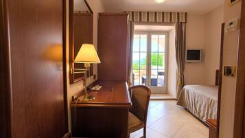 A hotel room with a wooden desk, a chair, a bed, a TV, and a view of the outdoors through a sliding door.