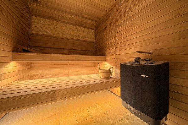 A sauna room with wooden walls and benches, a stone wall, and a black speaker. - Hotel Kanajt (Punat)