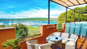 A terrace with wicker furniture, a potted plant, and a view of a marina. - Hotel Kanajt (Punat)