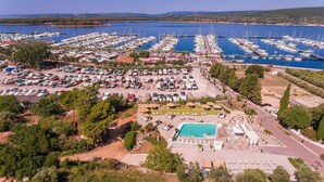 An aerial view of a marina with numerous boats docked, a swimming pool, and surrounding greenery. - Hotel Kanajt (Punat)