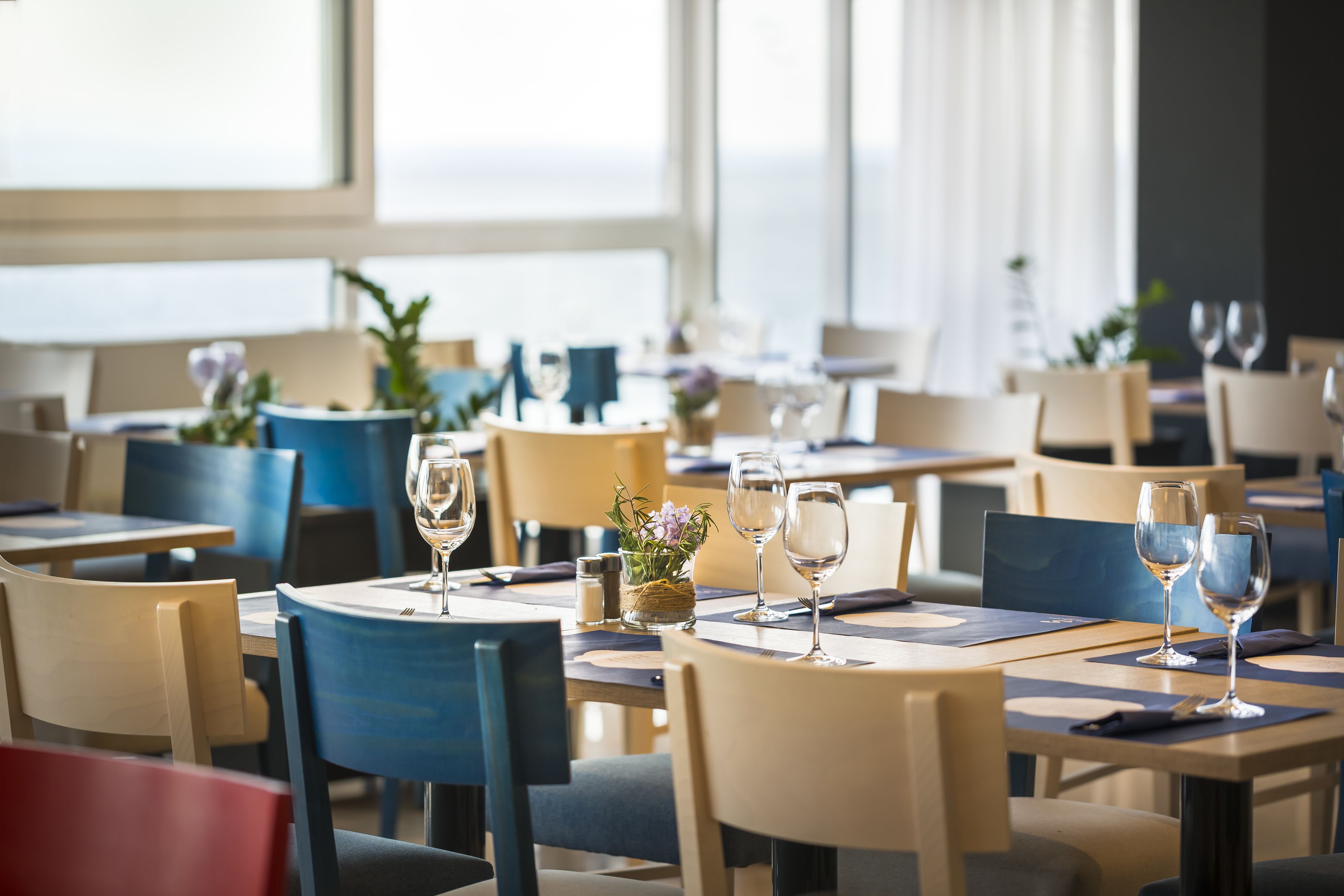 A restaurant with tables set for dining, chairs, and a view of the outdoors.