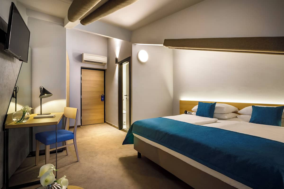 A hotel room with a bed, desk, chair, and a television.