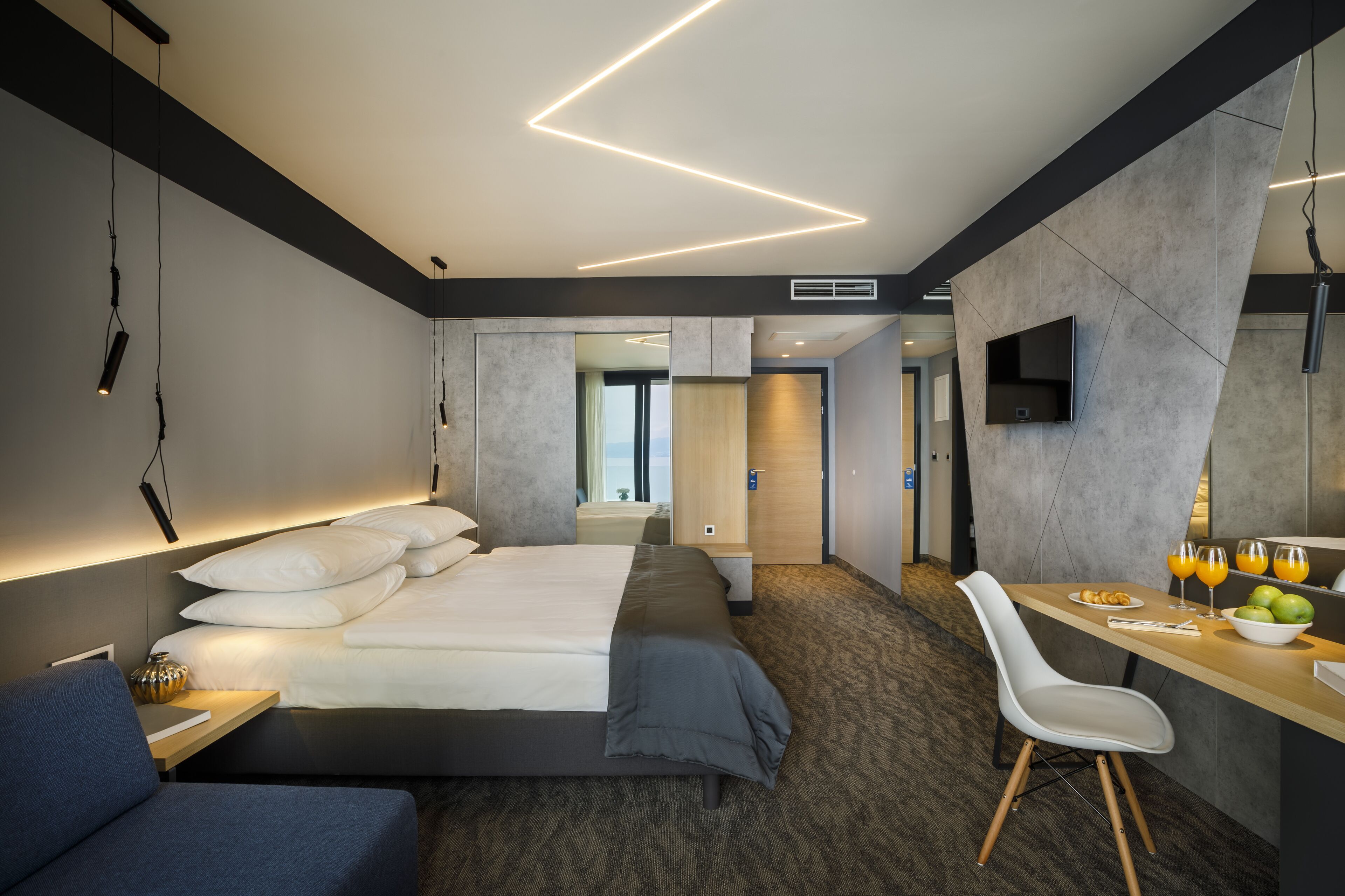 Moderni hotellihuone, jossa on suuri sänky, työpöytä tuolilla, taulutelevisio ja näkymä kaupunkiin.