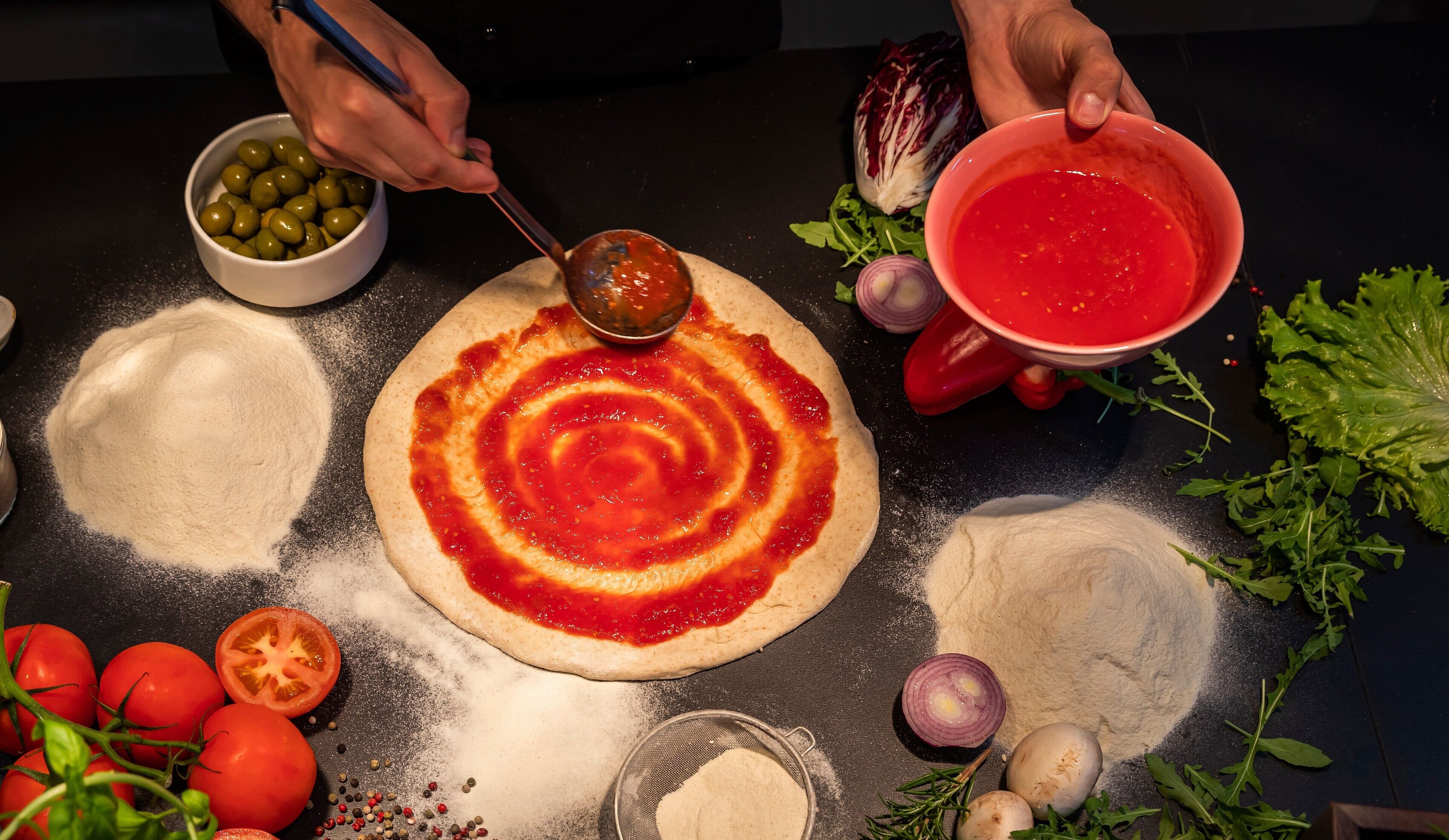 Pizza bereiding met diverse ingrediënten en gereedschap op een tafel.