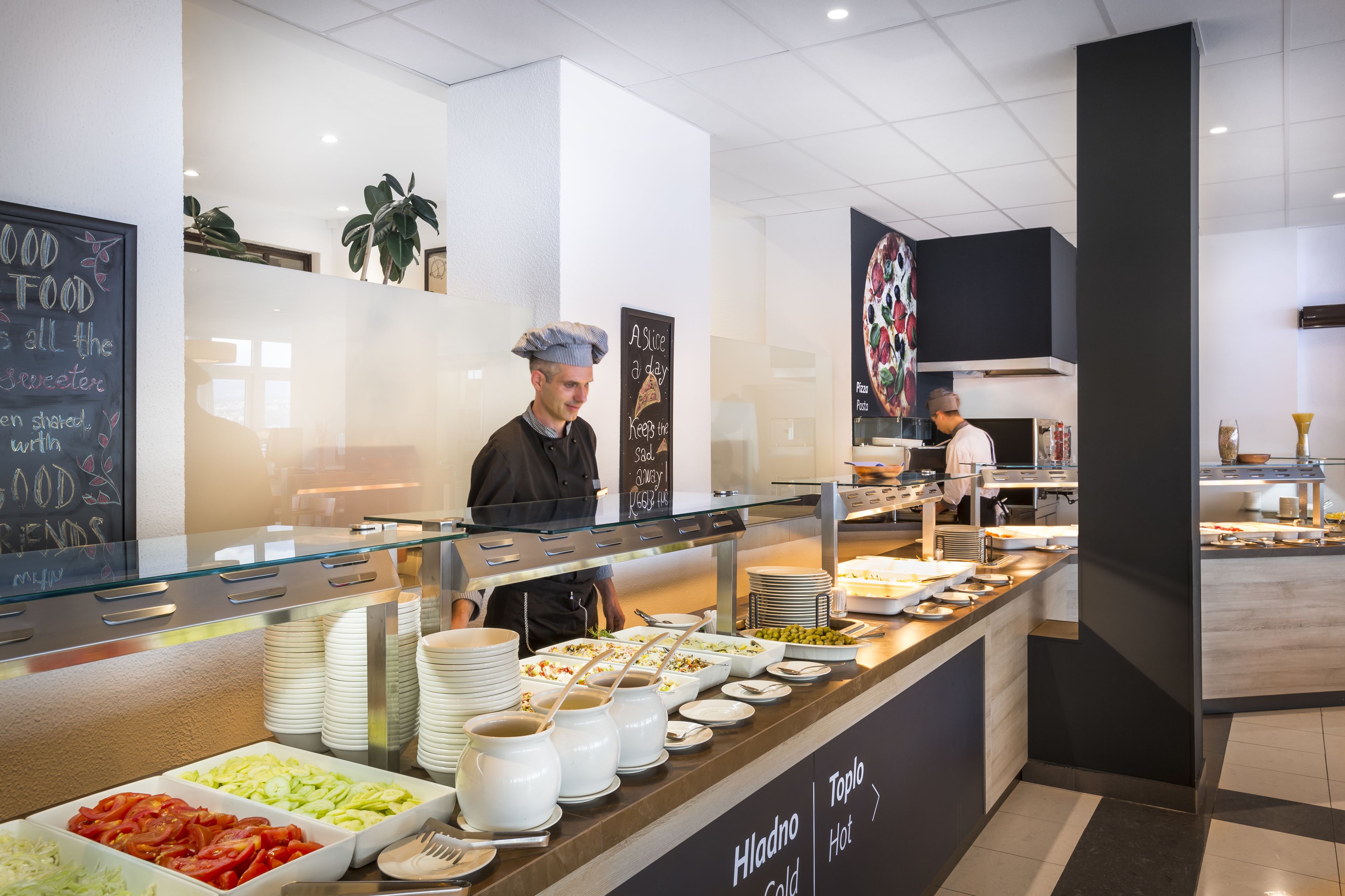 Zona de buffet con diversas opciones de comida, una pizarra con mensajes sobre gastronomía y un cocinero preparando alimentos.