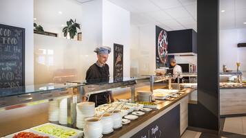 A buffet area with various food options, a chalkboard with food-related messages, and a chef preparing food.