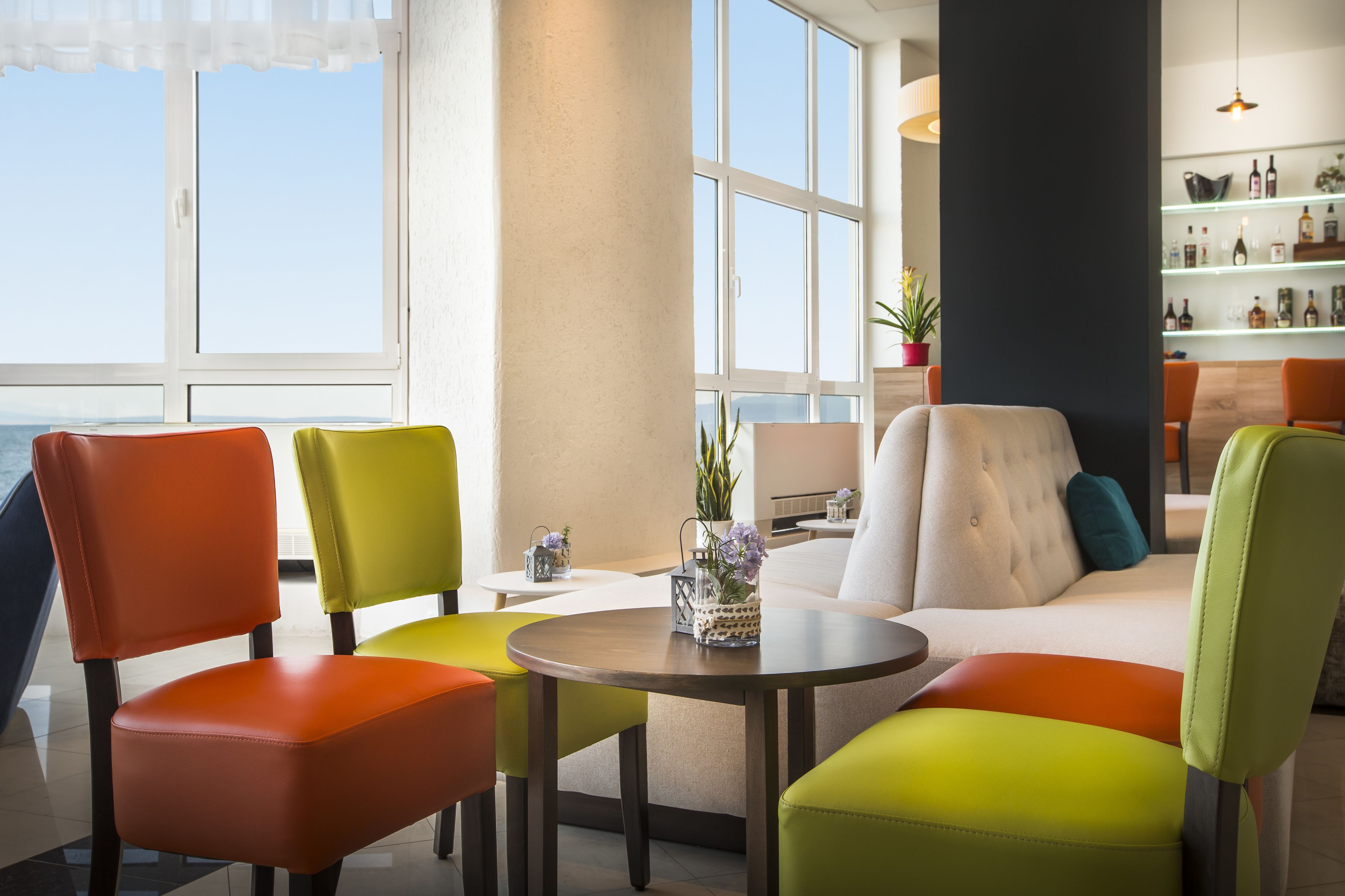 Un espace de détente moderne avec des fauteuils et un canapé aux couleurs vives, une table ronde et une vue sur la mer grâce à de grandes fenêtres.
