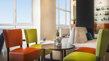A modern lounge area with colorful chairs and a sofa, a round table, and a view of the sea through large windows.