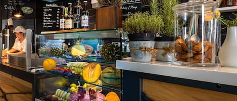 A food display with fruits and a chef preparing food behind a counter.