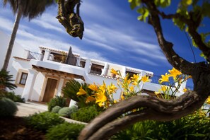 A white building with balconies, surrounded by greenery and yellow flowers. - Can Planells (Sant Joan de Labritja)