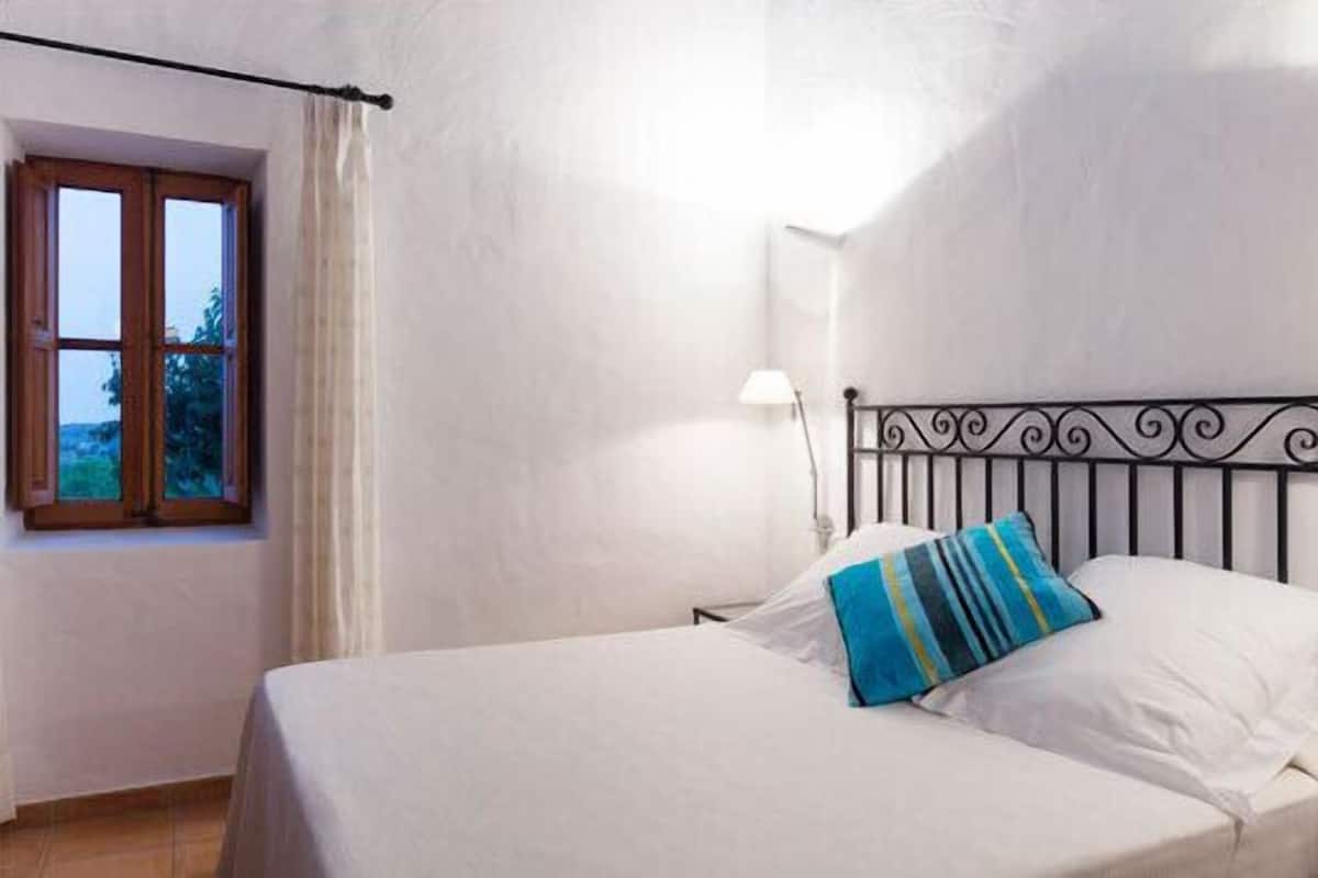 A bedroom with a bed, a window, and a nightstand.
