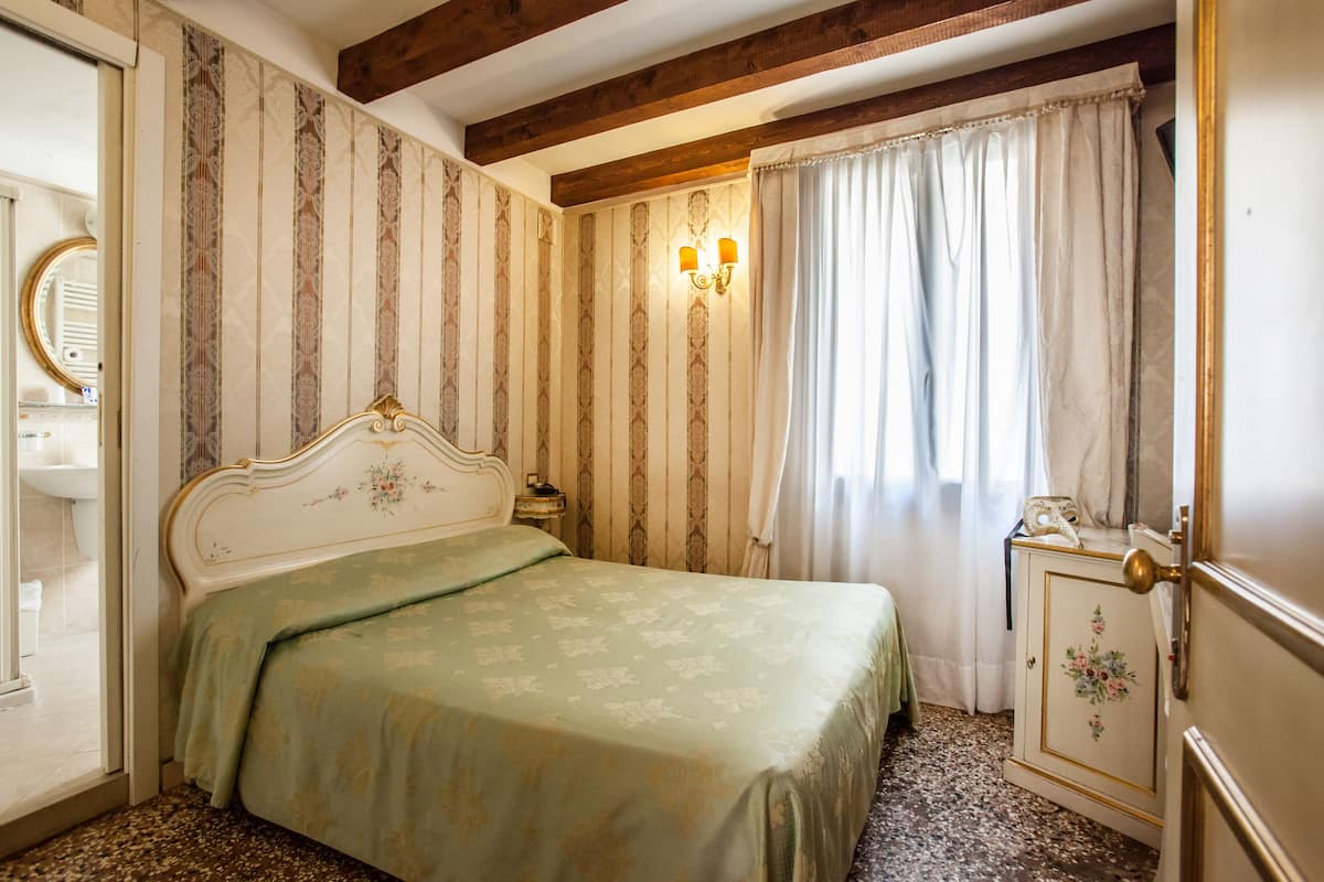 A bedroom with a bed, a nightstand, a dresser, a mirror, and a window with curtains.