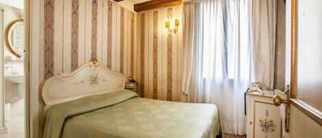 Une chambre à coucher avec un lit, une table de chevet, une commode, un miroir et une fenêtre avec des rideaux.