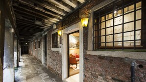 A corridor with exposed brick walls and a wooden ceiling. There is a sign for 'Locanda Barrarico' and a window with a grid pattern.