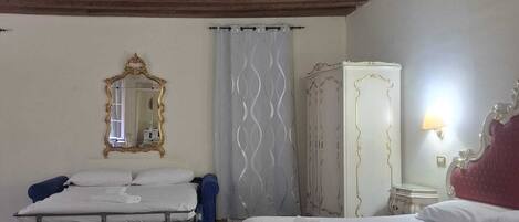 A hotel room with two beds, a large mirror, a wardrobe, and a ceiling with exposed beams.