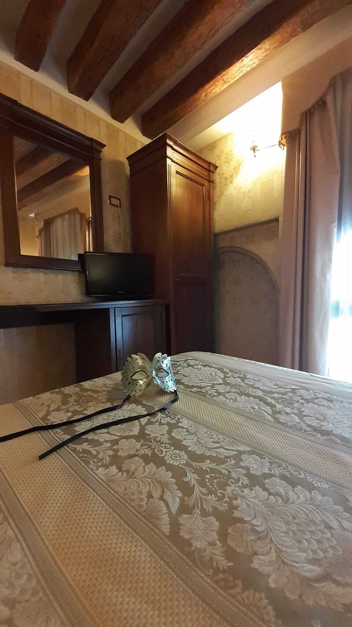 Une chambre à coucher avec un lit, une armoire en bois, un téléviseur posé sur une commode et un grand miroir.
