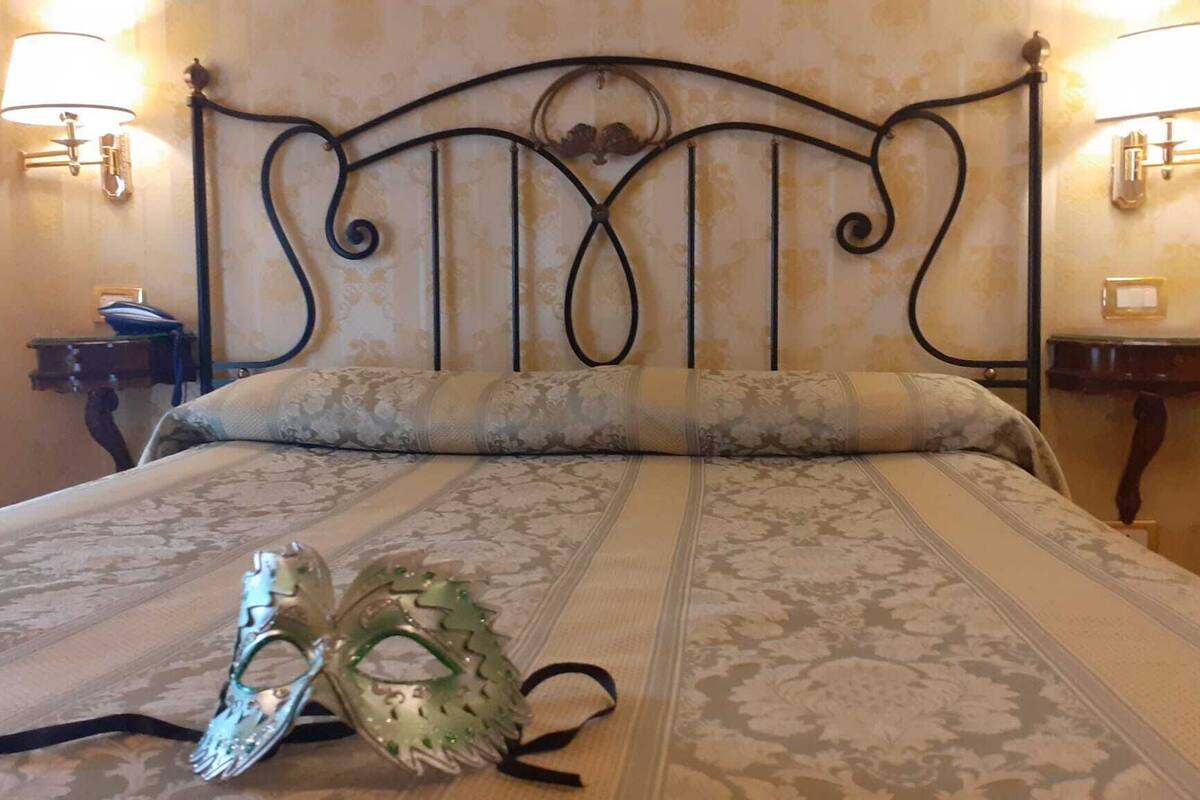 A bed with a metal headboard, two bedside lamps, and a decorative mask on the bed.