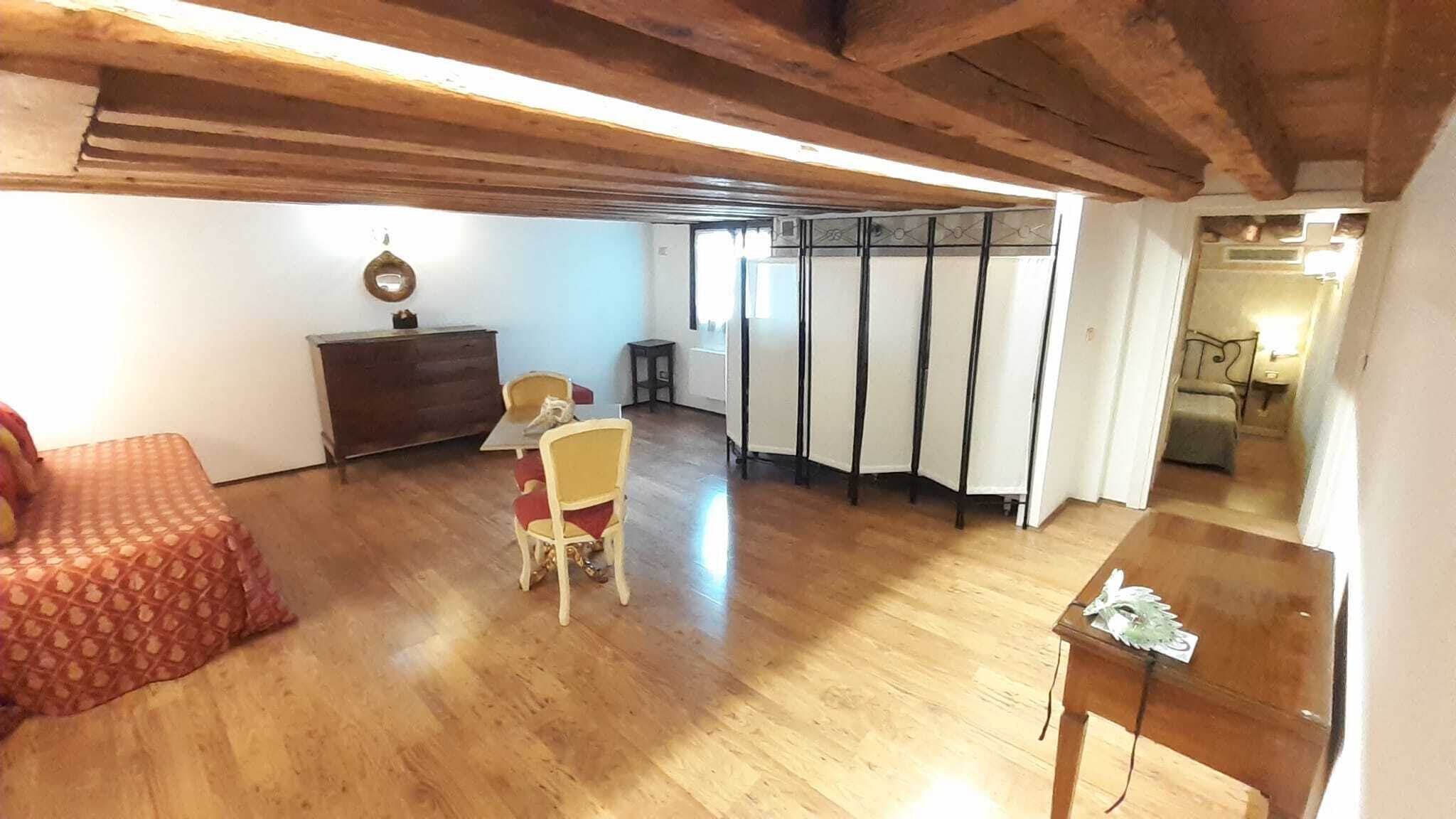 Una habitación amplia con pisos de madera, una zona de comedor con una mesa y sillas, un sofá y una pequeña mesa de madera.