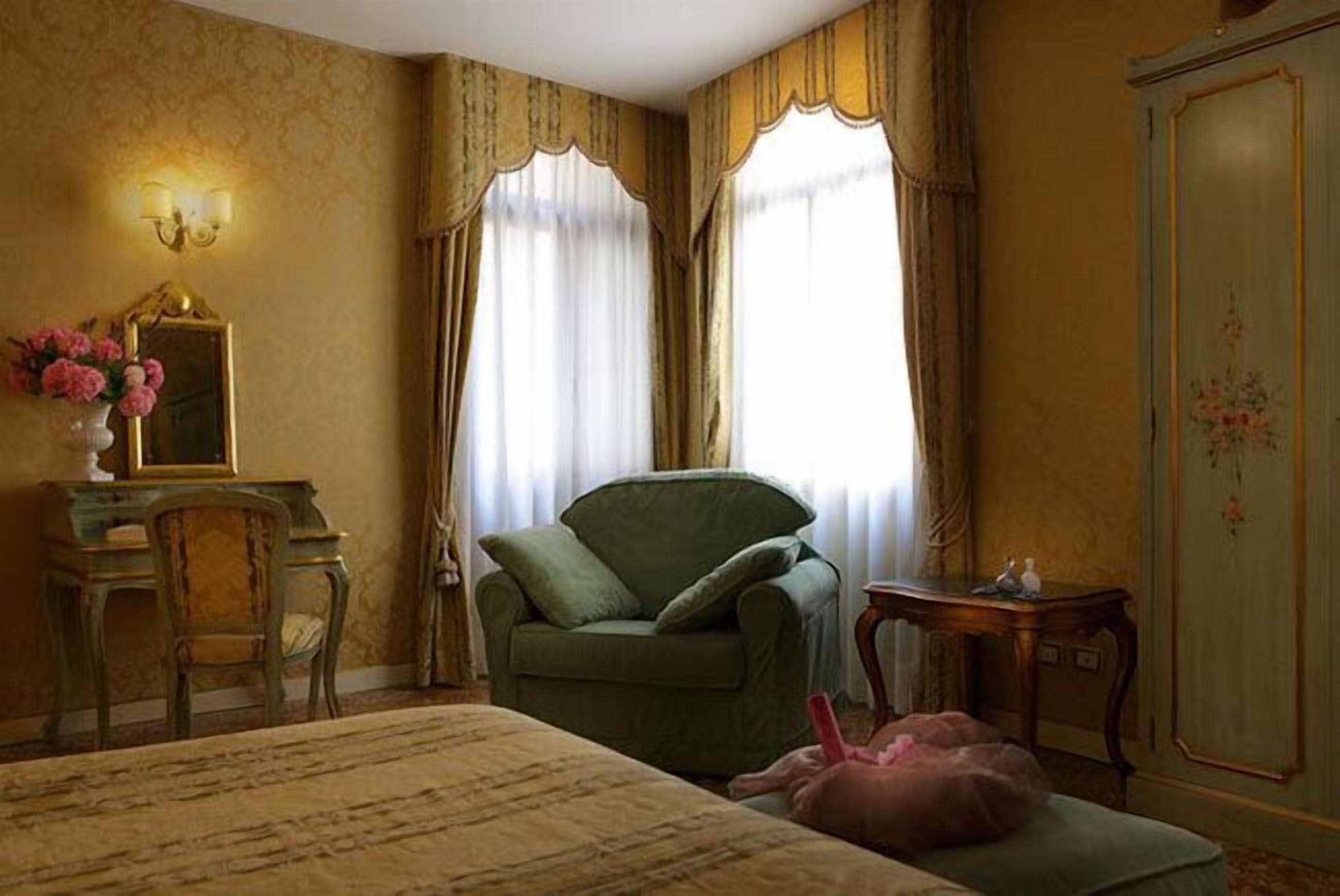 A room with a bed, a green armchair, a small table, and a mirror on a dresser.