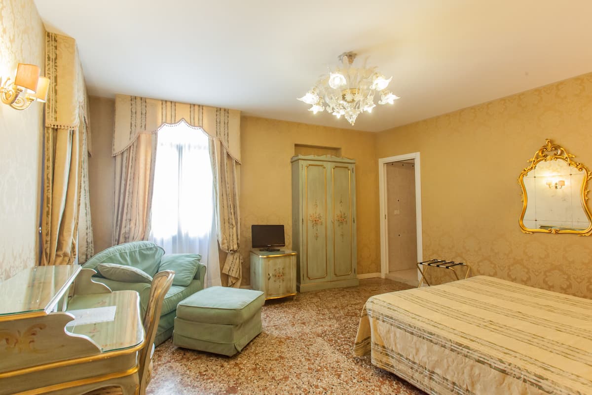 A room with a bed, a desk, a chair, a television, a wardrobe, and a chandelier.