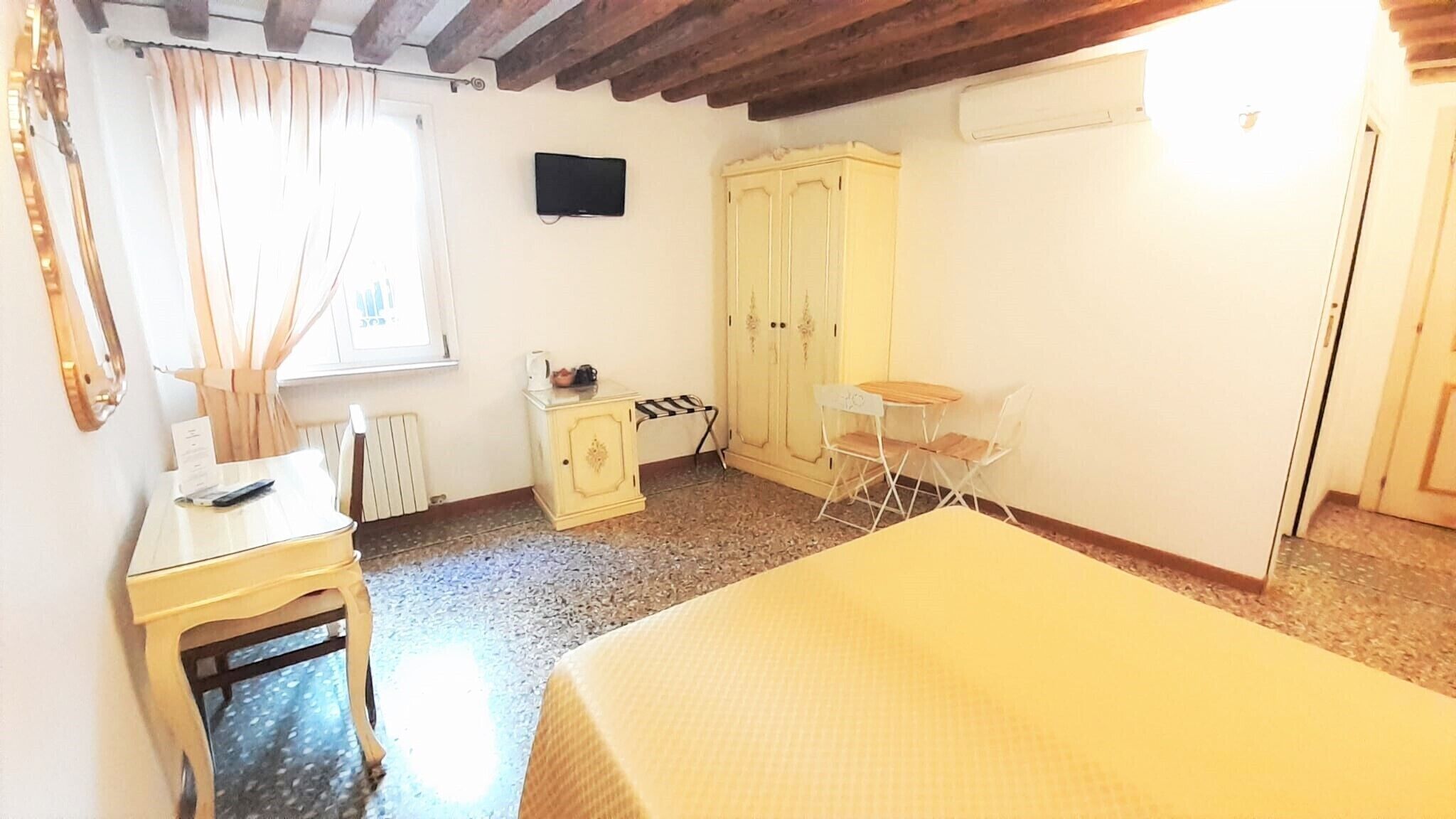 A small, well-lit room with a bed, a desk, a chair, a wardrobe, and a radiator.