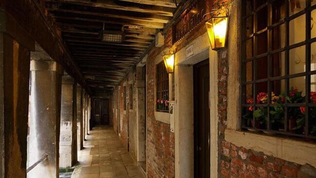 A corridor with brick walls, wooden beams, and a tiled floor.