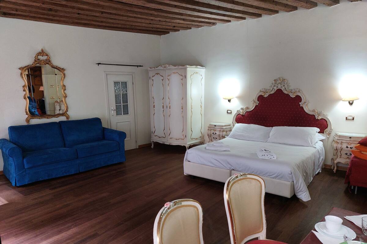 A hotel room with a bed, a blue sofa, a wardrobe, and a mirror.