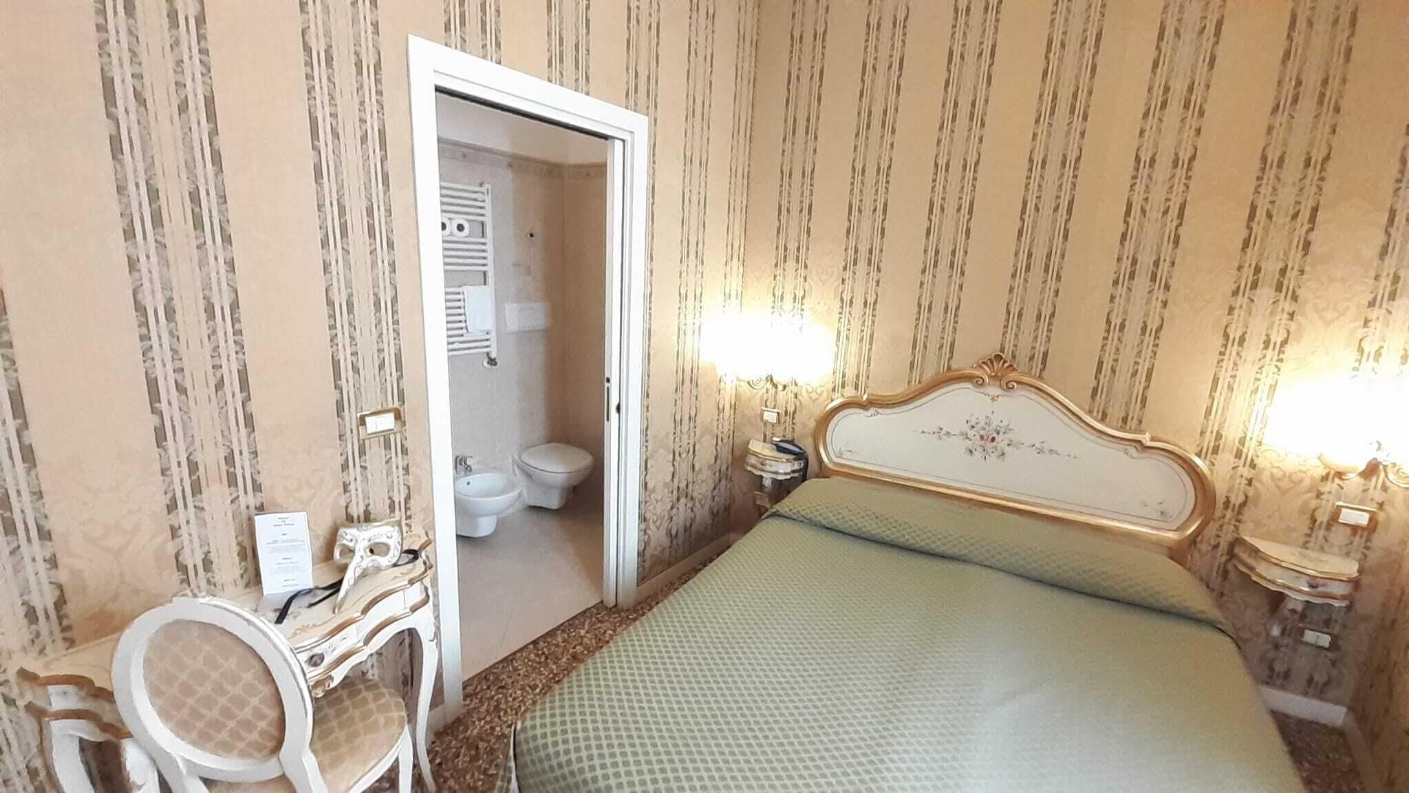 A bedroom with a bed, a nightstand, a dresser, and a bathroom visible through an open door.