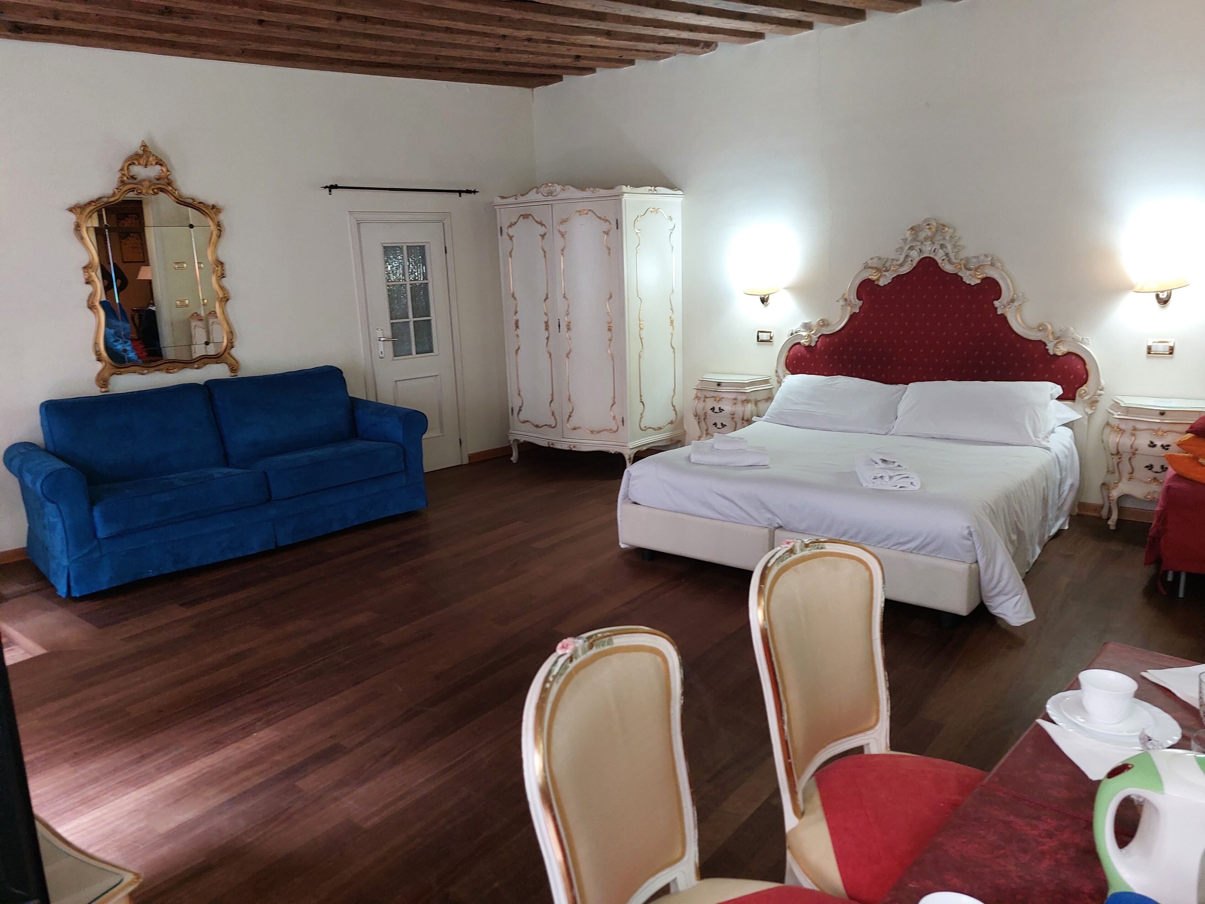 A bedroom with a bed, a blue sofa, a wardrobe, and a mirror.