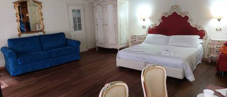A bedroom with a bed, a blue sofa, a wardrobe, and a mirror.