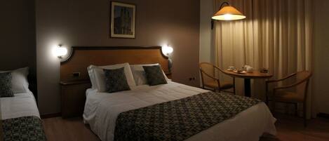 A hotel room with a large bed, two bedside tables, a chair, a small table with a lamp, and a painting on the wall.